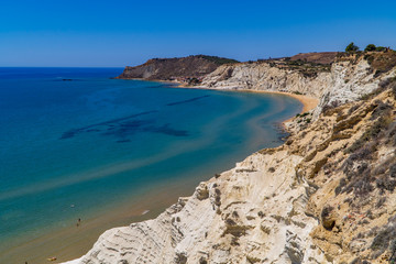 Obraz premium White limestone cliffs with beaches, swimmers, and different shades of blue seas at the Scala dei Turchi in Sicily, Italy