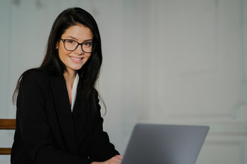 Glasses for vision. A student is sitting studying on a laptop. A young female accountant works remotely in a coworking space. Stylish black comfortable suit.