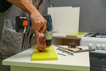 furniture assembly service. employee installs a handle on a furniture door. worker drills a hole for attaching a furniture door handle