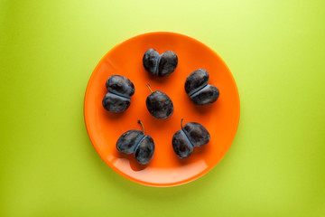 Orange plate with ugly plums or prunes on green background