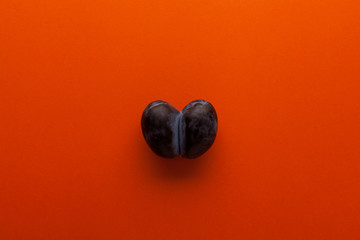 Ugly fruit on a coral background with copy space. Heart-shaped prunes or double plums