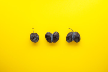 Ugly fruits on a yellow background with copy space. One normal plum and two intergrown double prunes - obrazy, fototapety, plakaty