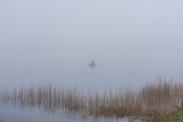 Autumn landscape with a fisherman on the lake in the fog. Early morning on the lake. A lone fisherman in a boat. A thick, gray morning fog. Relaxation in nature.