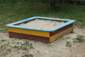 colored square wooden sandbox with white sand stands on the ground and green grass in the...