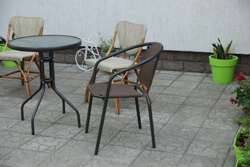 round brown table with chairs stand on the gray sidewalk against the wall in the street