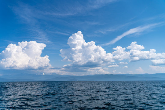 Russia, Irkutsk region, Baikal lake, July 2020: beautiful blue sky with wooly white clouds over smooth water