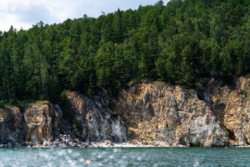 Naklejka na ściany i meble Russia, Irkutsk region, Baikal lake, July 2020: stone mountains with evergreen forest on them, from water view