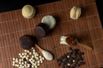 maizena alfajores with coconut white and dark chocolate with dulce de leche and wooden spoon with sweet caramel on wooden bottom
