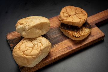 
homemade whole and sliced ​​burger potato bread toasted on wooden board on black background