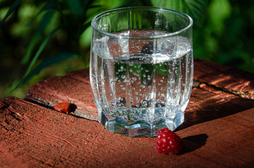 A glass with mineral, carbonated water raspberry berry, on a wooden board in the garden.