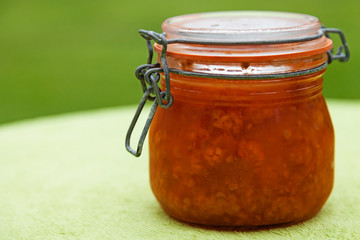 a glass jar with cloudberry jam on green background