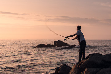 Young professional fisherman casts his rod (spin technique), trying to fish while the sun goes down in a good fishing point of northwest of Spain, next to Portuguese border.