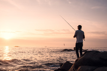 Young professional fisherman casts his rod (spin technique), trying to fish while the sun goes down in a good fishing point of northwest of Spain, next to Portuguese border.