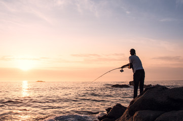 Young professional fisherman casts his rod (spin technique), trying to fish while the sun goes down...