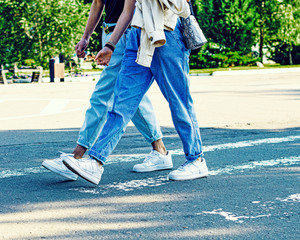 Legs Of Two millenials In Jeans And Comfortable white cross shoes. urban casual street style fashion sunny day