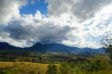 Dramatic dark clouds over distant blue mountain; Motion blur in the foreground; Golden hills illuminated by afternoon sun.