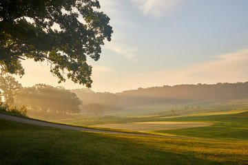 Early morning sunrays shining through the trees and fields on a beautiful golf course