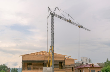 Reconstruction of a wooden building. The fast-erecting tower crane works by lifting the load. Sky background with clouds.