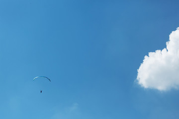 Blue Paraglider flying into the sky with clouds on a sunny day