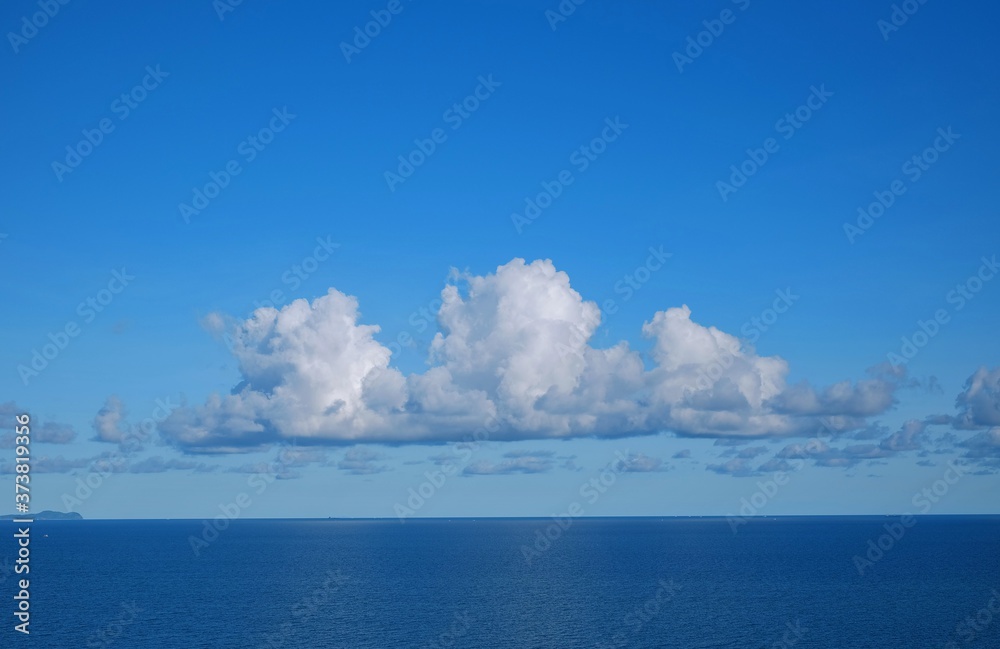 Wall mural view of a calm blue sea with white fluffy clouds and clear blue sky on a sunny day in early morning 