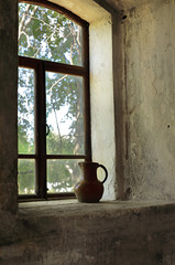 Still life with an old clay jug on the window in a village abandoned house.