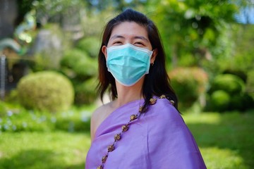 A young Asian woman with traditional Thai costume is wearing a surgical mask while walking in a...
