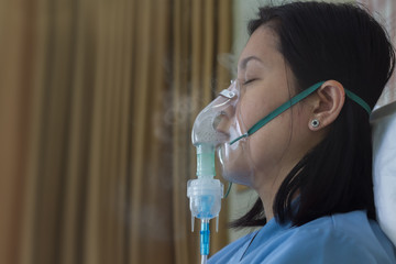 Sickness female in blue clothe wearing nasal mask with respiratory problem in hospital room. Asian...