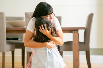 Happy mother embracing her lovely daughter with both hands. Young Caucasian mom sitting on floor with adorable little boy girl in living room and smiling. Leisure, family and parenthood concept © Mangostar