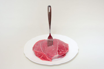 Raw beef meat steak with fork in it on white plate on light background . Carnivore, keto