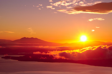 夜明けの空に力強く輝く太陽。津別峠、北海道。Abstract of sunrise and sunset. The sun is shining in the sky,clouds flowing low,lake surface seen in thin light.Scenic view from high place. Tsubetsu-pass,hokkaido,japan.