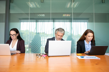 Businesspeople working at computers in meeting room, using laptops at conference table. Medium shot, front view. Communication or wireless technology concept