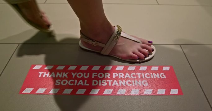 Tourist steps on red floor sign at hotel reminding to practicing social distancing. Woman feet in summer shoes is walking in hotel lobby by COVID-19 prevention signage. Safe travels during coronavirus