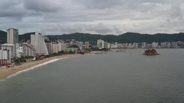 Vista a&eacute;rea panor&aacute;mica de la zona hotelera de la bah&iacute;a de Acapulco, el drone volando sobre el oc&eacute;ano a baja velocidad hacia el morro Farall&oacute;n del Obispo