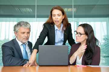 Confident project manager showing presentation to colleagues. Businesswoman standing at open laptop in meeting room, speaking and explaining content details to partners. Communication concept