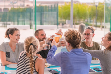 a group of smiling young people doing a toast over a table on an out of focus background. Friendship and lifestyle concept.
