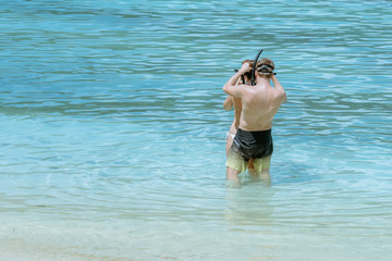 A gentleman helped wear glasses for his lover before snorkelling to see the beautiful coral in the sea.