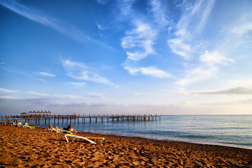 Obraz premium View from sand beach to water of sea, pier and silhouette of people or tourists in a nice day or evening with blues sky and white clouds.