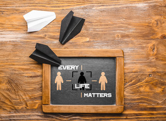 Chalkboard with text EVERY LIFE MATTERS and different paper airplanes on wooden background. Racism concept
