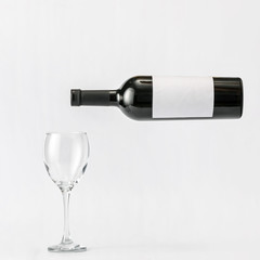 Fototapeta premium Bottle of wine with blank label and glass on light background