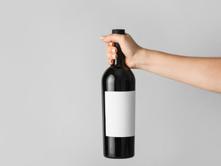 Hand holding bottle of wine with blank label on light background. Mockup for design