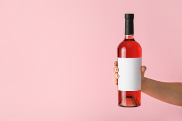 Hand holding bottle of wine with blank label on color background. Mockup for design