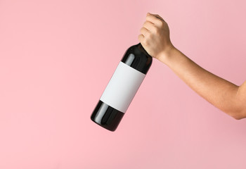 Hand holding bottle of wine with blank label on color background. Mockup for design