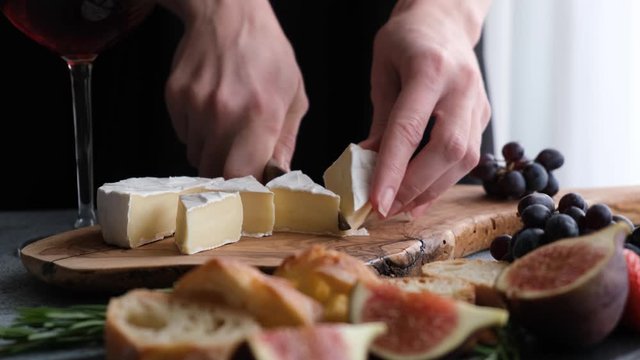 Brie or camembert cheese with figs and grapes. Woman cutting soft cheese camembert to make a cheese platter