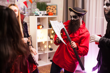 Bearded man dressed up like a pirate holding an axe while celebration halloween with his monster...