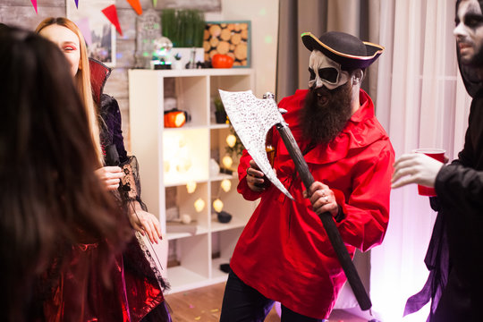 Bearded man dressed up like a pirate holding an axe while celebration halloween with his monster friends.