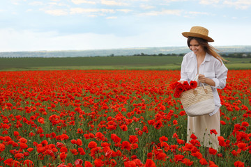 Woman holding handbag with poppy flowers in beautiful field