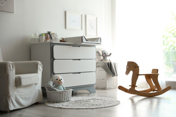 Beautiful baby room interior with toys, armchair and modern changing table