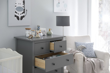 Modern open chest of drawers with baby clothes and accessories in room