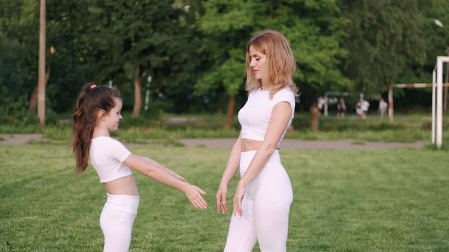 Sporty mother and her daughter are oing exercises outdoors. The active family is having fun together. They are clapping each other's hands.