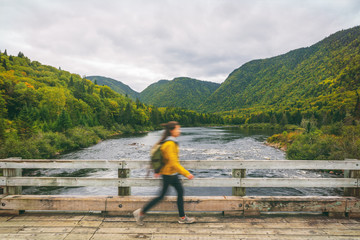 Fototapeta na wymiar Hiker woman with backpack walking on bridge crossing river. Motion blur of tourist hiking in outdoor nature fall. Autumn traveling hike in Quebec, Canada.